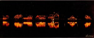 Several boathouses on the Schuylkill River lit up as if for Christmas, with lights outlining the buildings and reflected in the water