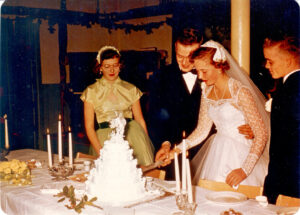 Wedding party wit bride and groom cutting cake while maid of honor and best man watch on