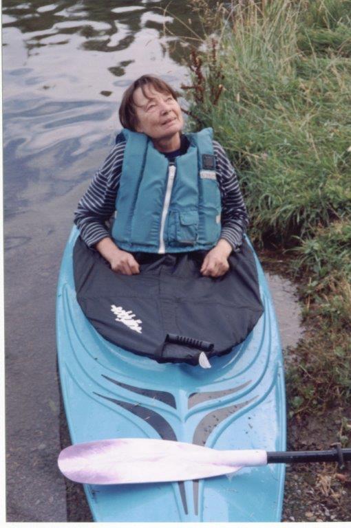 Holly Lucas sits in her kayak at the bank of a river with her head back smiling.