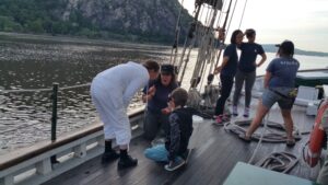 Woman and young boy examine a young eel in a bucket on the on the deck of the Clearwater.