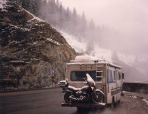 Recreational Vehicle covered with snow on a pullover in the mountains which are also covered with wno.